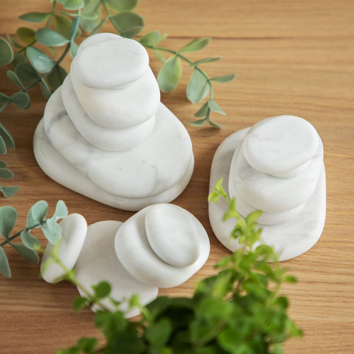 Verschillende witte, ovale stenen op houten ondergrond, gerangschikt. Groene planten op de achtergrond.