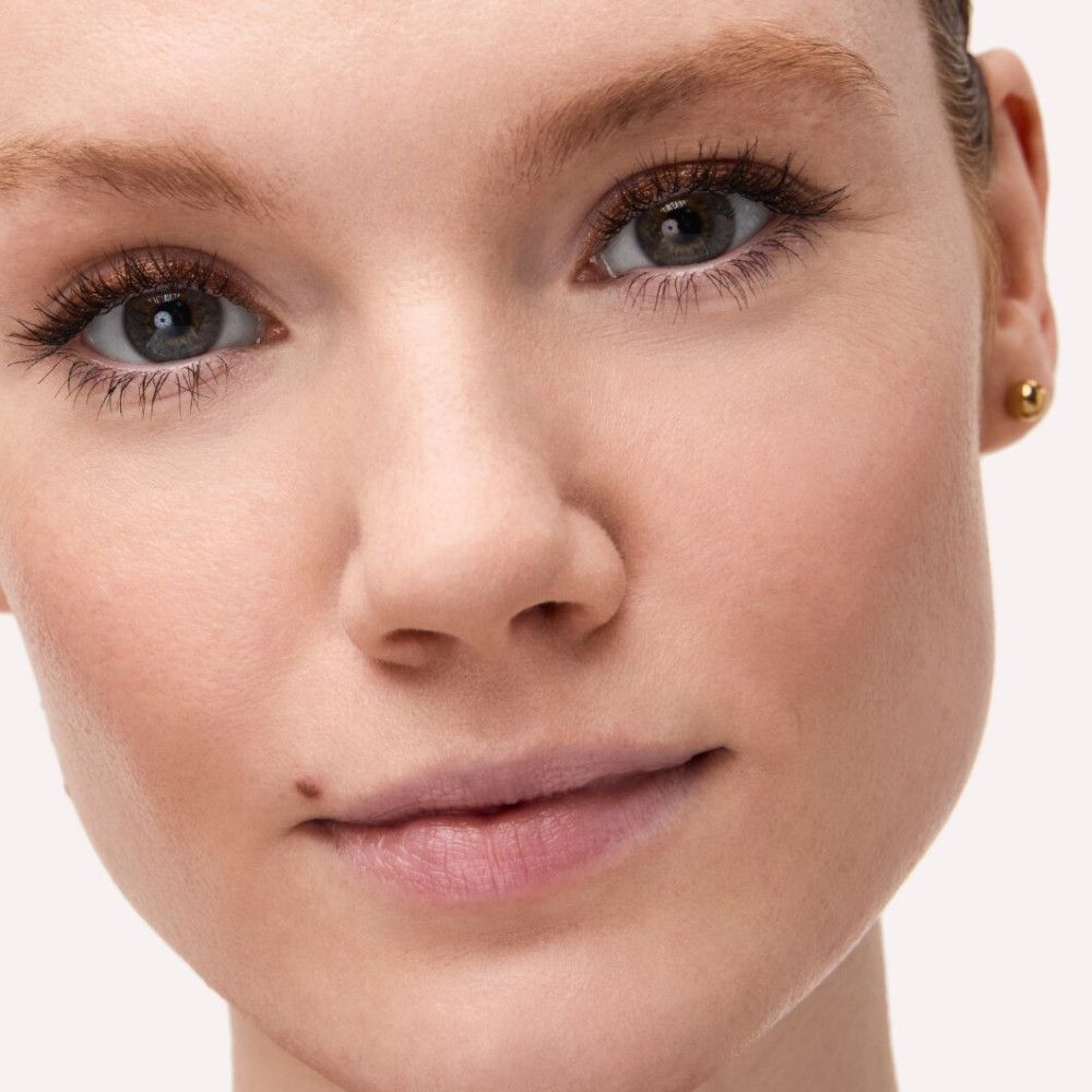 Gros plan d'un visage. Teint, sourcils, cils et yeux. Boucle d'oreille dorée.