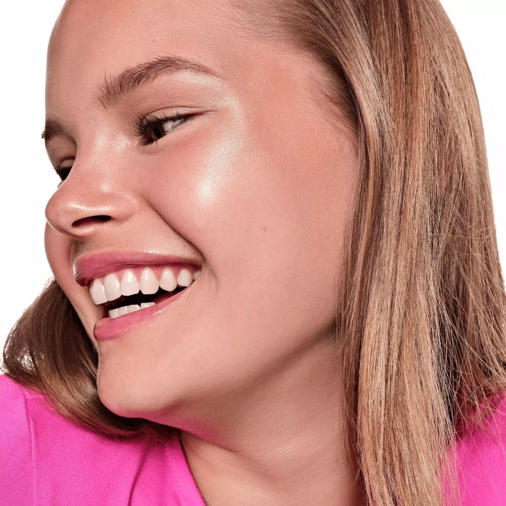 Portrait d'une femme souriante avec highlighter sur la peau. Haut rose. Peau brillante.