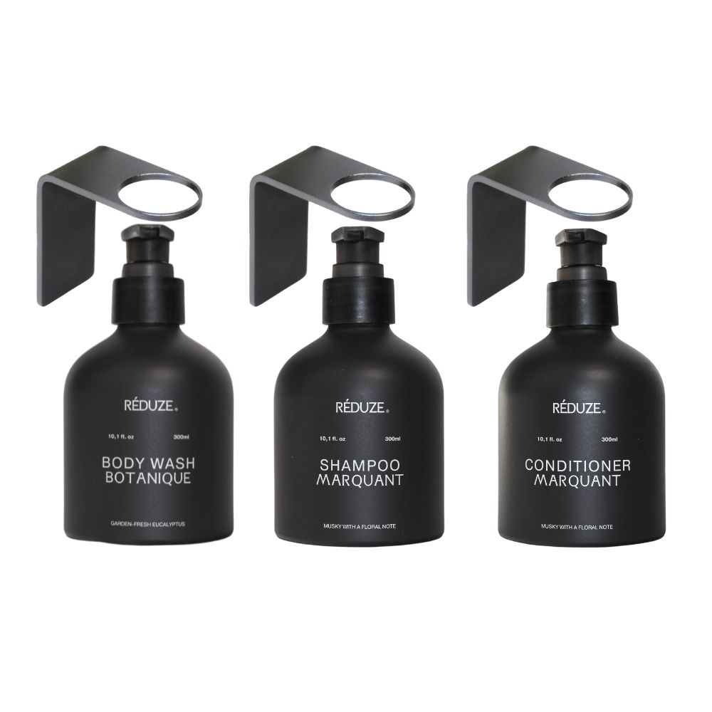 Drie zwarte flessen met pomp en wandhouder. Labels: Body Wash, Shampoo, Conditioner. Merk: RÉDUZE.