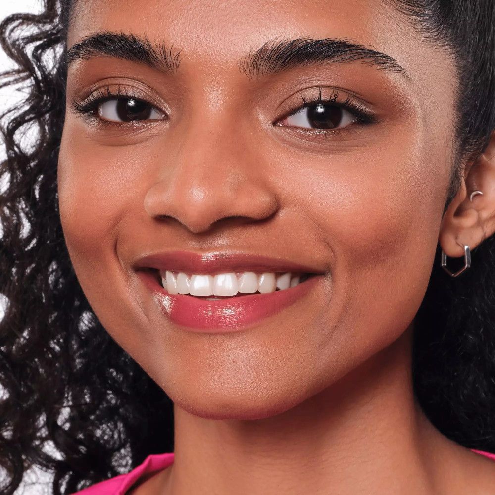 Gros plan d'une femme avec un Lip Tint rose. La femme sourit. Elle a la peau foncée et porte des boucles d'oreilles.