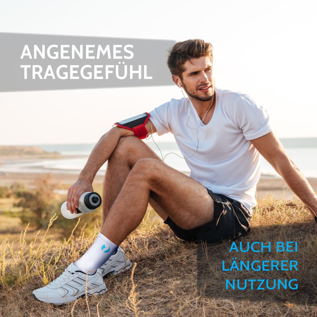 Man zit op strand met enkelbrace. Wit product met blauw logo. Voor langdurig gebruik.