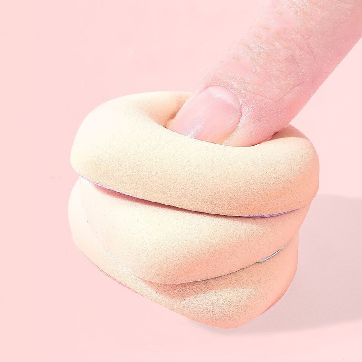 Une éponge de maquillage beige clair est comprimée par un doigt. L'éponge est douce et flexible.
