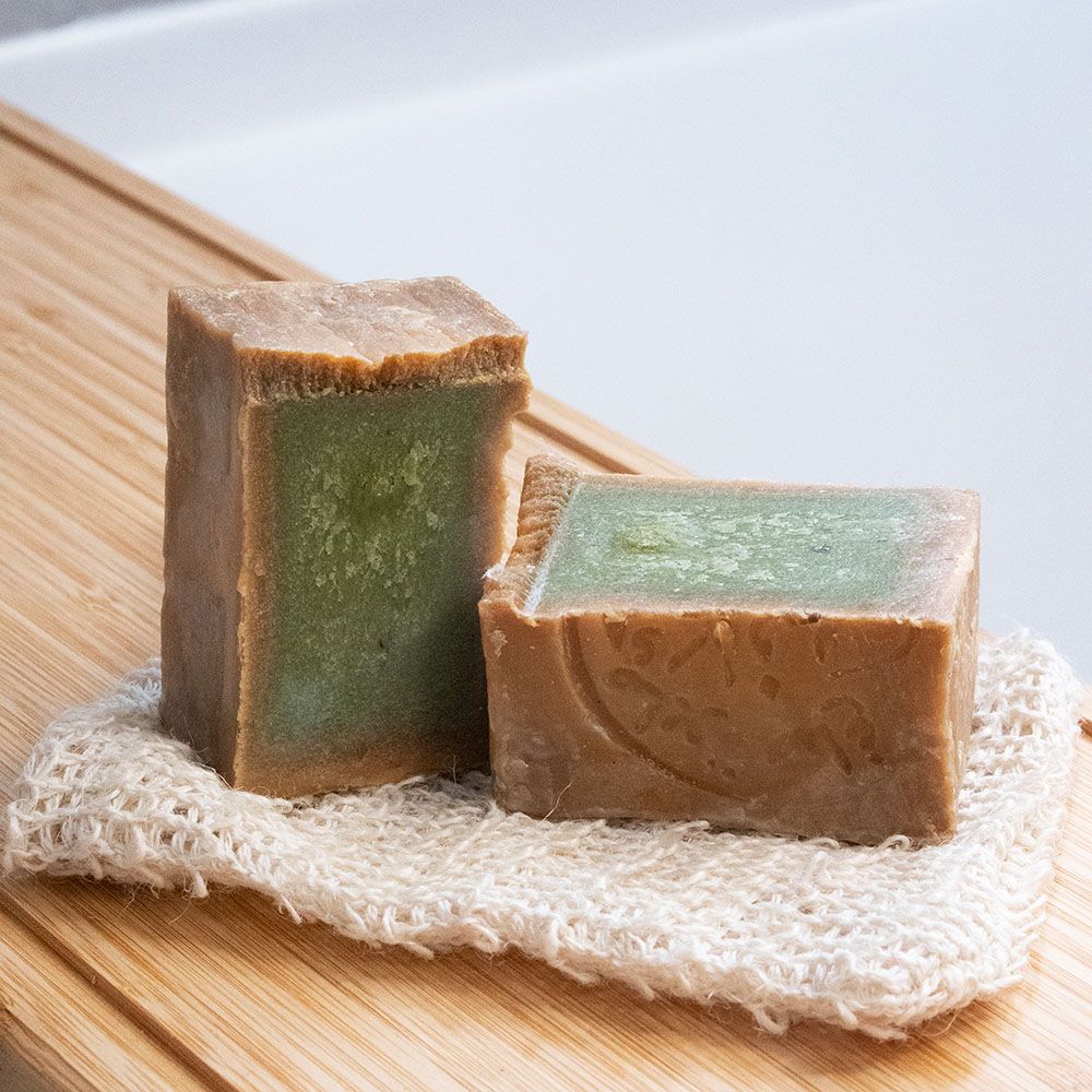Deux savons rectangulaires, intérieur vert. Sur un gant de toilette. Sur planche de bois.