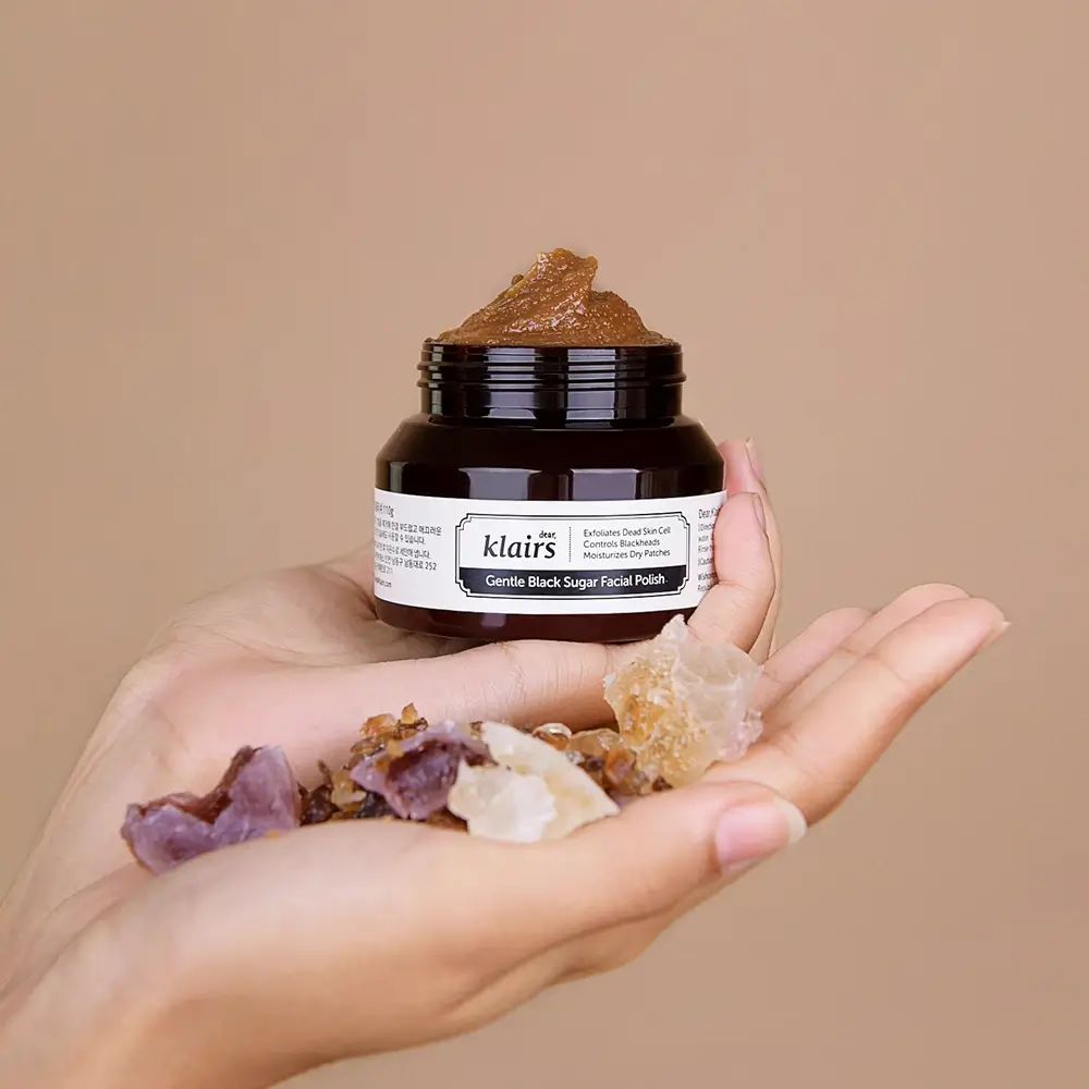 Potje bruine crème in handen. Stenen ernaast. Opschrift: Klairs Gentle Black Sugar Facial Polish.