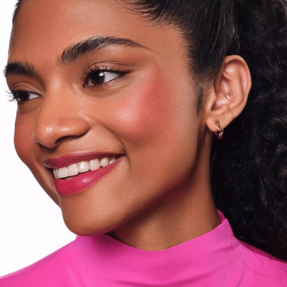 Gros plan d'une femme avec lèvres et joues roses. Elle porte un haut rose et a les cheveux foncés.