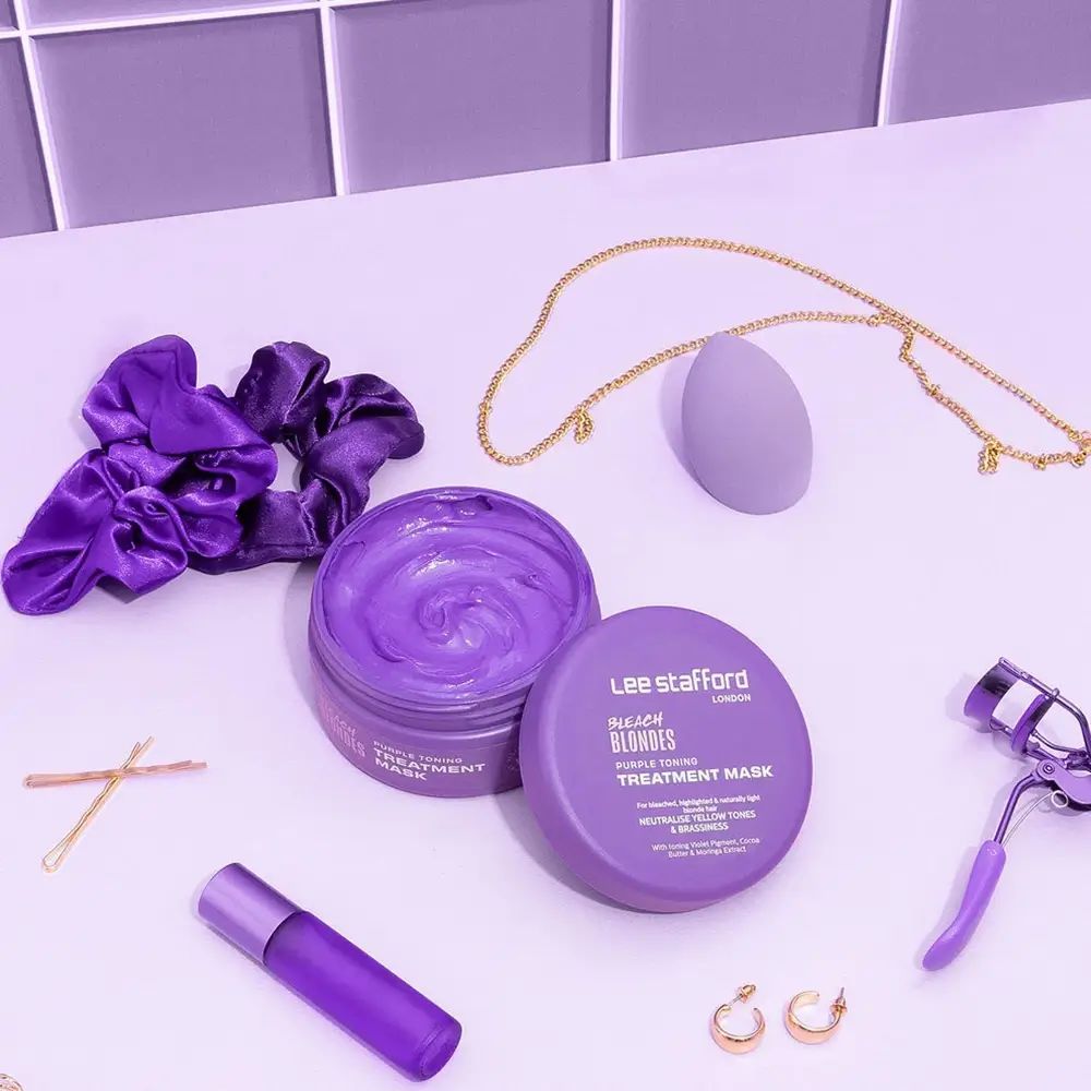 Twee open paarse potten met product, omringd door accessoires: scrunchie, sieraden, wimperkruller.