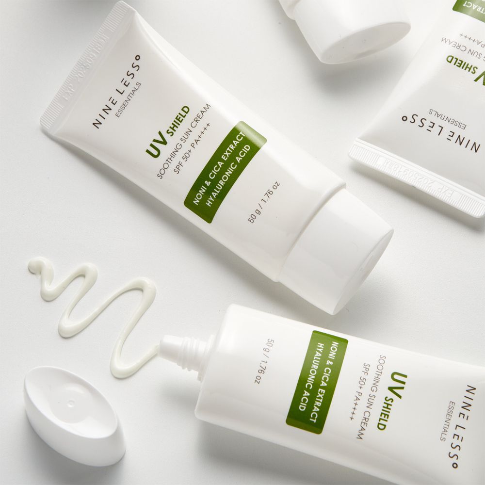 Meerdere witte tubes en crème op witte achtergrond. Opschrift: UV Shield, SPF 50+ PA++++, Noni & Cica Extract, Hyaluronzuur. Merk: NINE LESS.