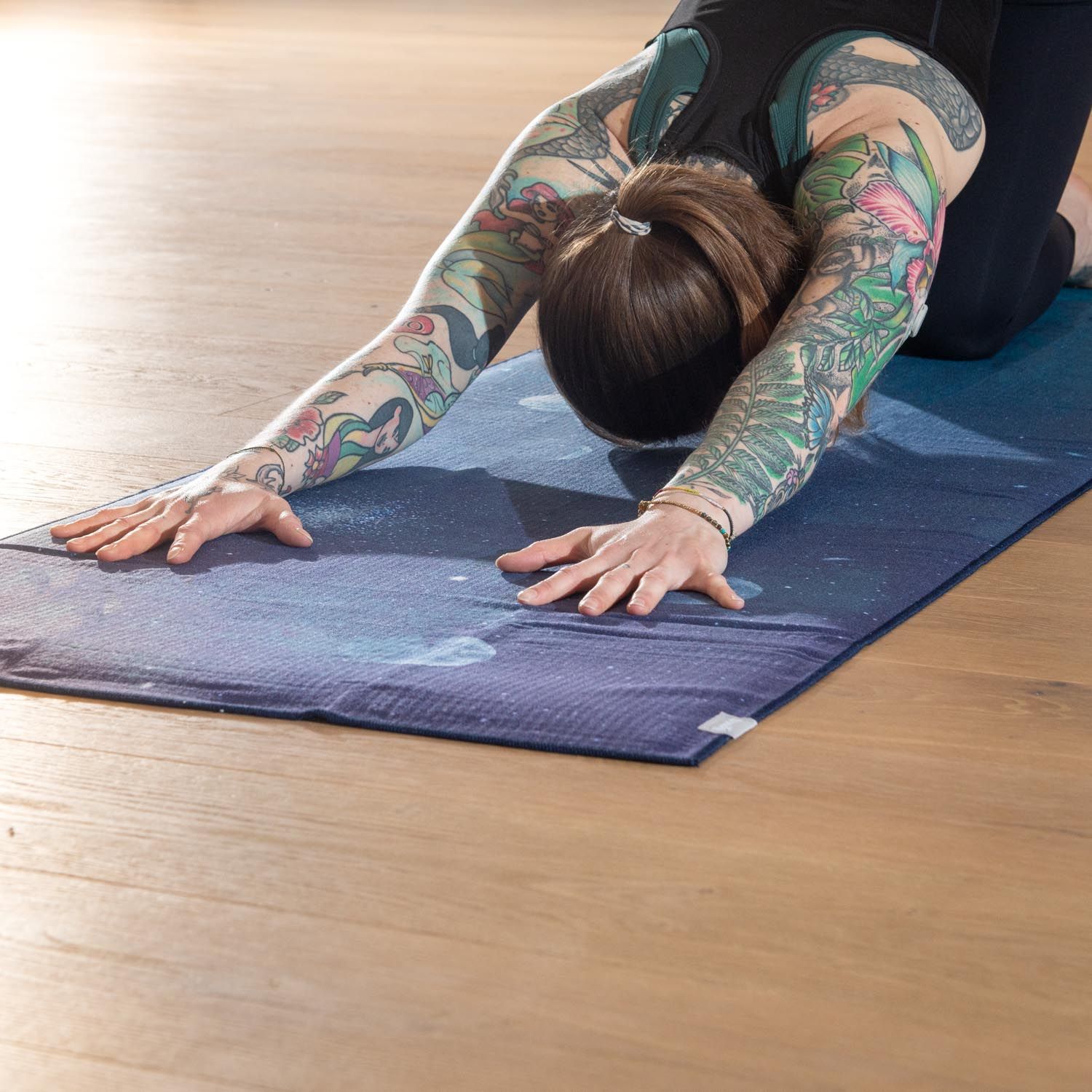 Persoon in yoga positie op yoga handdoek, nightblue, maan ontwerp. Op houten vloer.