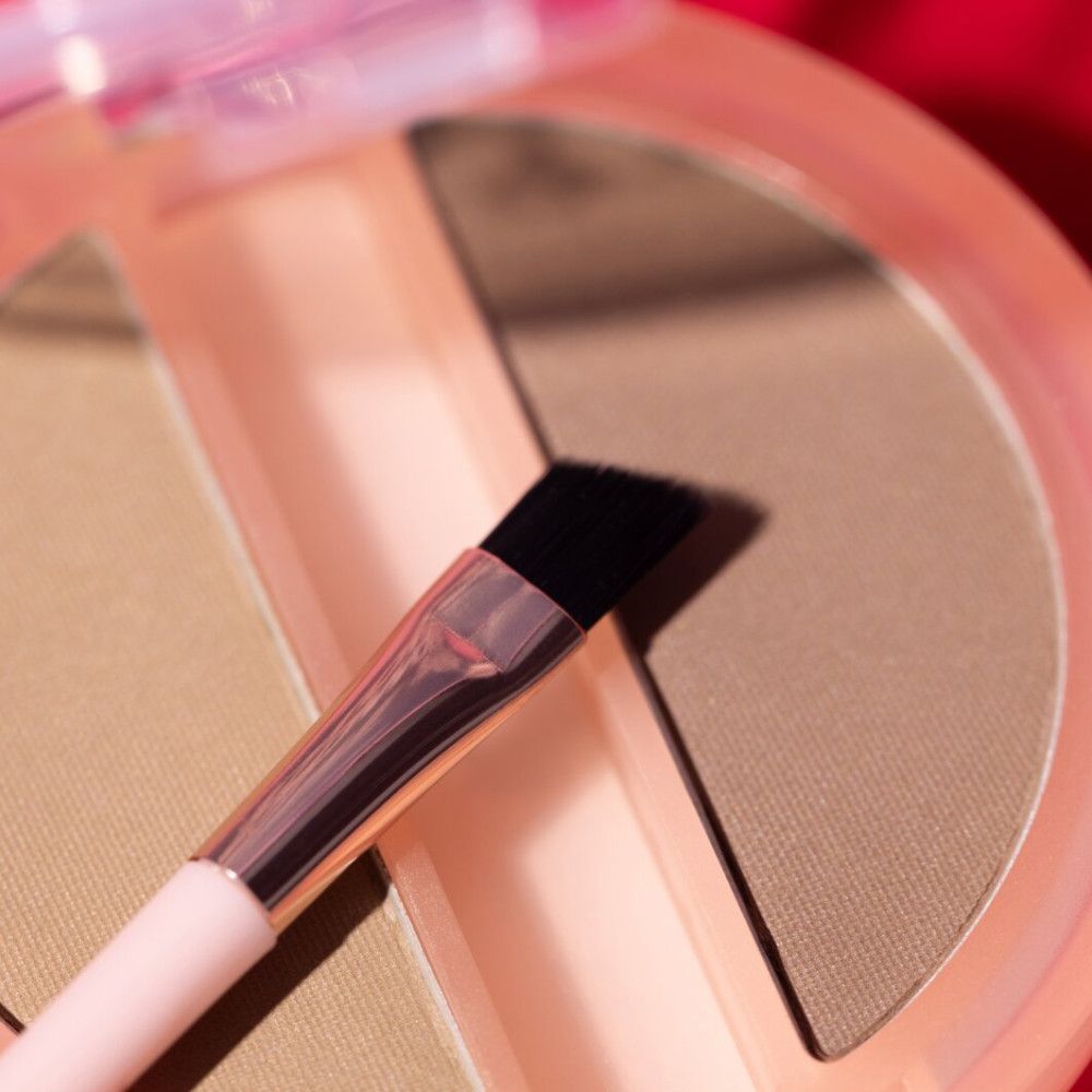 Gros plan du duo de poudres à sourcils. Pinceau avec tête de poils noirs. Emballage rose. Tons bruns.