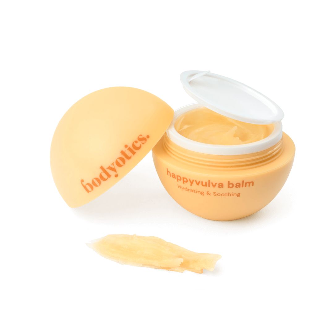 Baume beige dans un récipient rond avec couvercle. Inscription: happyvulva balm, bodyotics. À côté, une noisette de crème.