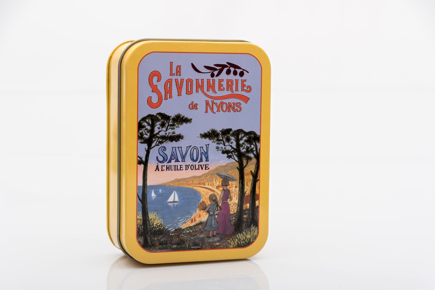 Boîte métallique jaune fermée. Sur le couvercle : "La Savonnerie de Nyons" et paysage. Forme rectangulaire.