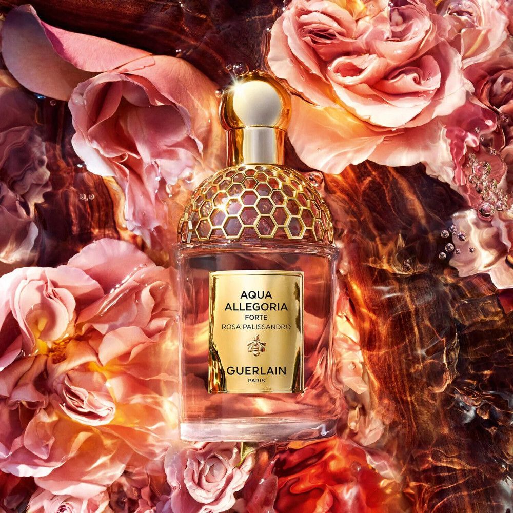 Flacon de parfum dans l'eau avec des roses. Bouchon et étiquette dorés. Nom du produit et logo visibles.