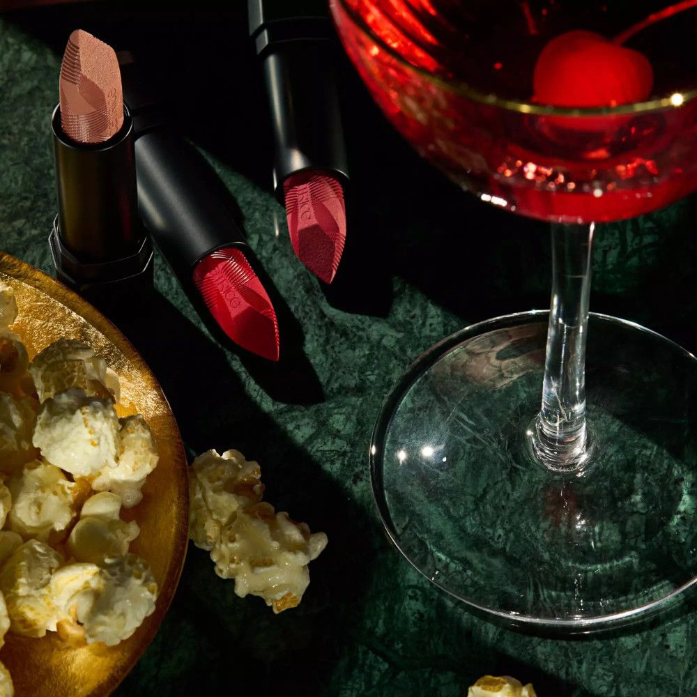 Trois rouges à lèvres à côté de pop-corn et d'un cocktail.
