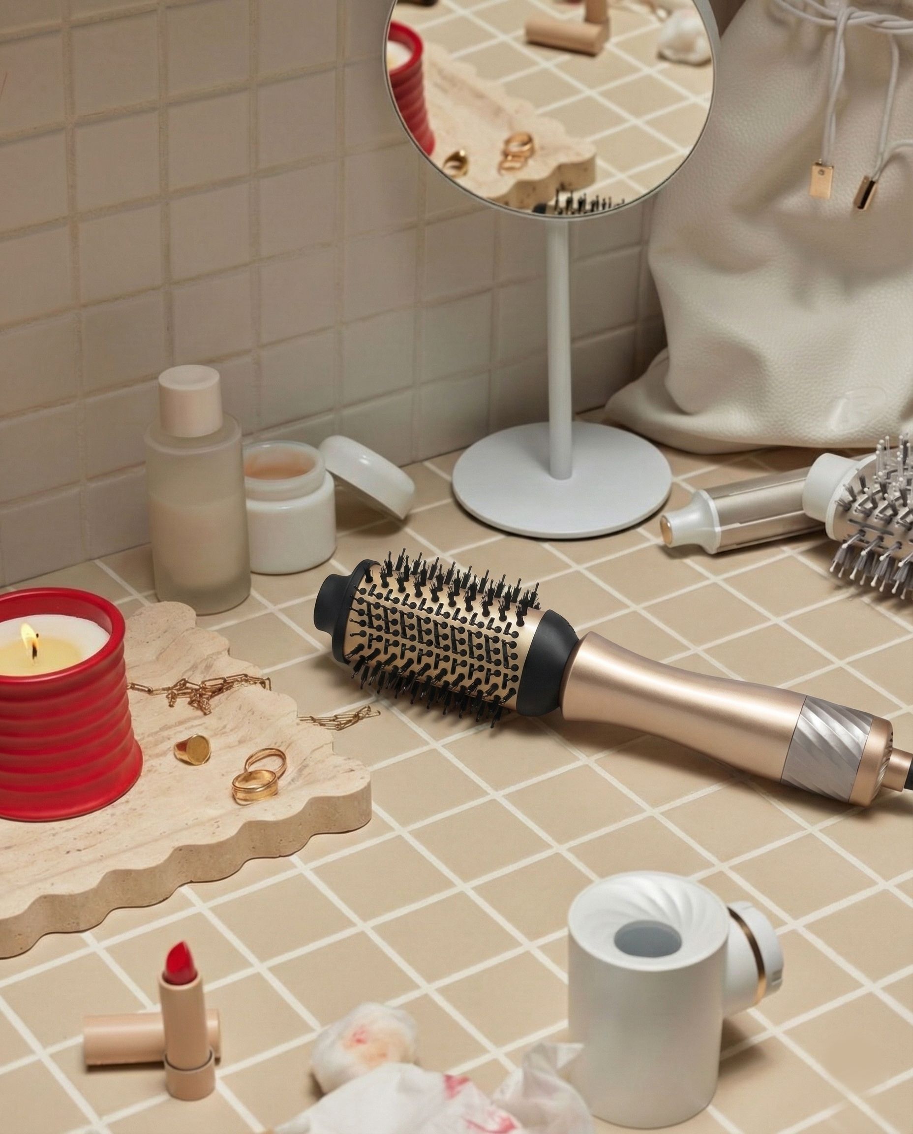 Gouden stylingborstel ligt op een betegeld oppervlak naast cosmetica en kaarsen.