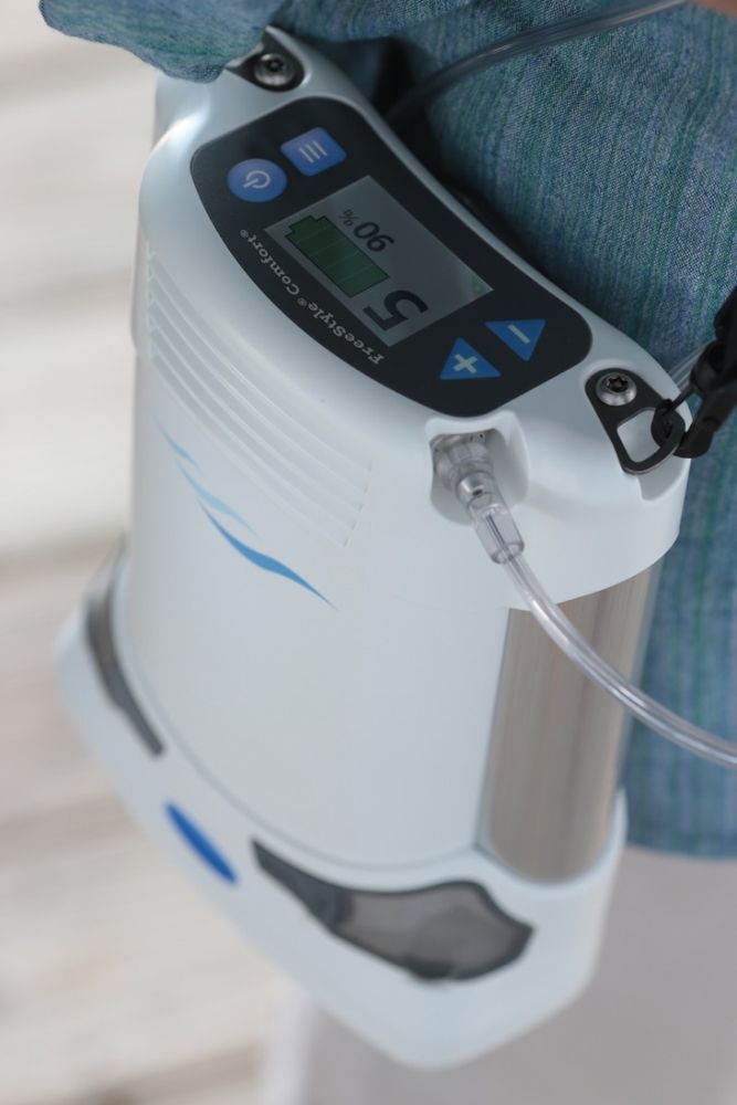 Draagbare zuurstofconcentrator in gebruik. Wit apparaat met display, gedragen. "FreeStyle Comfort"-logo.