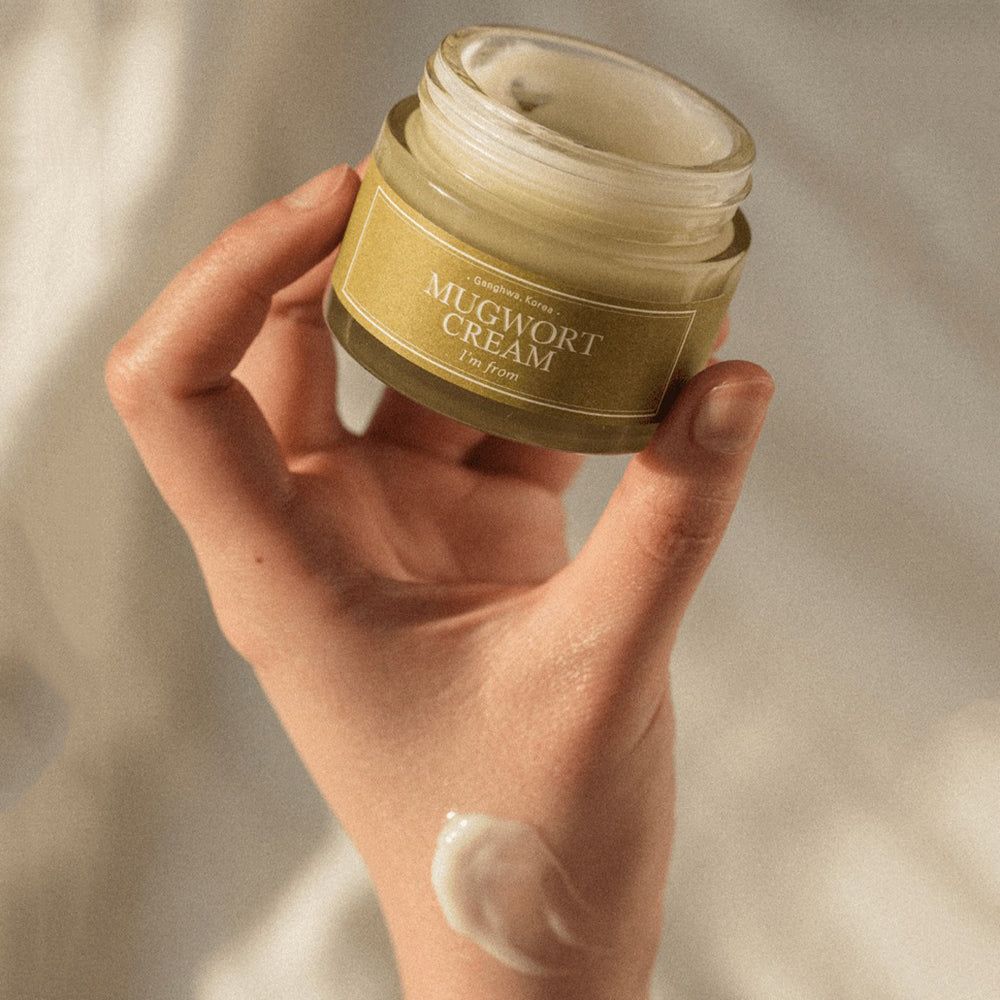 Main tenant un pot ouvert. Inscription : Mugwort Cream, I'm from. Goutte de crème sur la main.