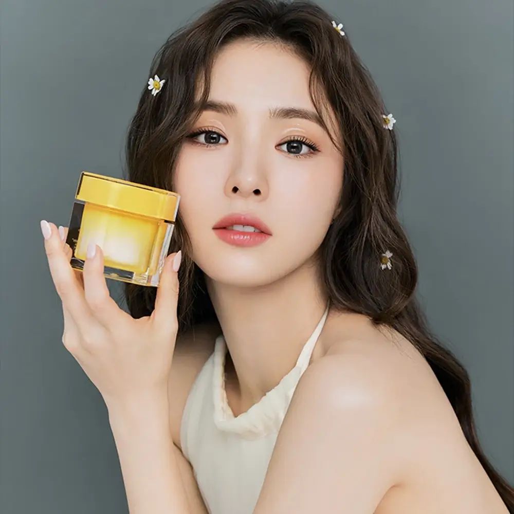 Femme tenant un pot de crème jaune transparent. Produit de soin du visage. Couvercle jaune, pot transparent. Femme avec des fleurs.