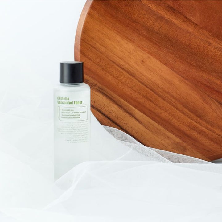Tonerfles met zwarte dop op houten plank en witte stof. Tekst: Centella Unscented Toner.