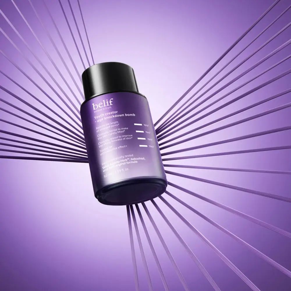 Paarse fles met zwarte dop, omringd door paarse lijnen. Opschrift: belif, Youth creator - age knockdown bomb. Product op paarse achtergrond.