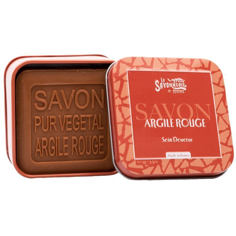 Boîte métallique ouverte avec savon à l'argile rouge. Inscription : La Savonnerie de Nyons, Savon Argile Rouge, Soin Douceur. Savon à côté.