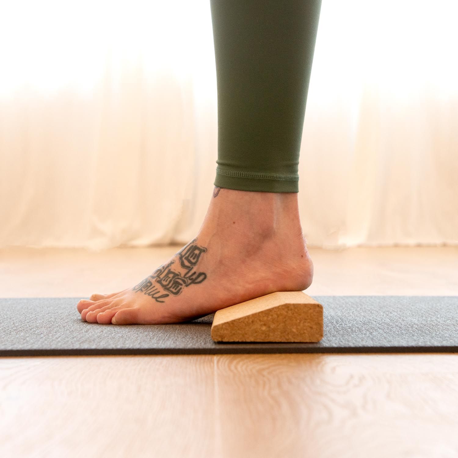 Pied sur la planche de handstand en liège sur un tapis de yoga. Jambe tatouée. Couleur marron.