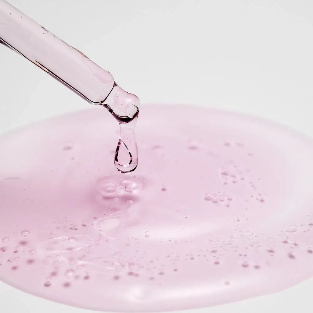 Pipet met roze vloeistof die in een plas druppelt. Vloeistof met belletjes.