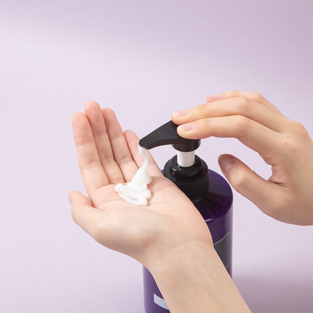 Handen die KUNDAL Honey & Macadamia Protein Treatment uit een pompfles knijpen.
