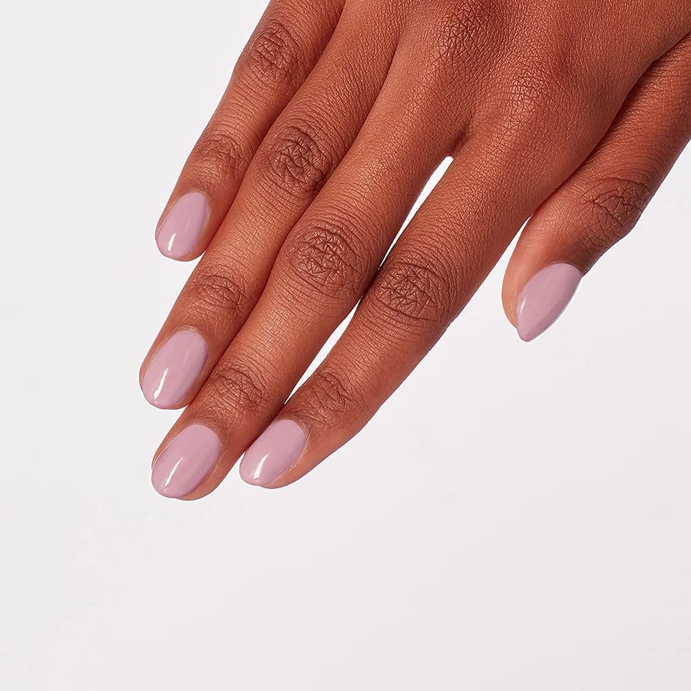 Hand met gelakte nagels. De nagels zijn ovaal en gelakt in een lichte roze tint. Op een lichte achtergrond.