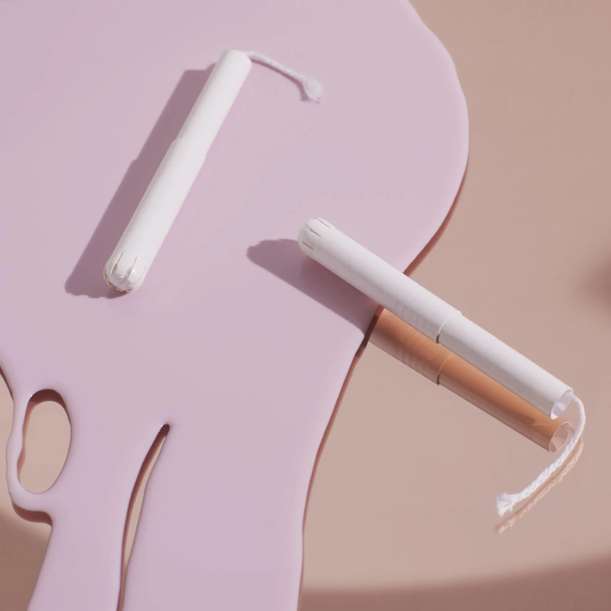 Deux tampons blancs avec applicateur sur surface rose. Un tampon avec fil.