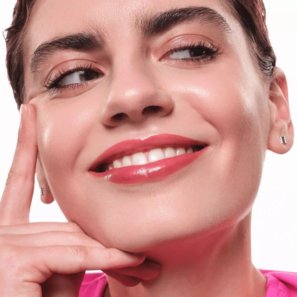 Gros plan d'une femme avec un Lip Tint. Les lèvres sont roses. La femme sourit et touche son visage.