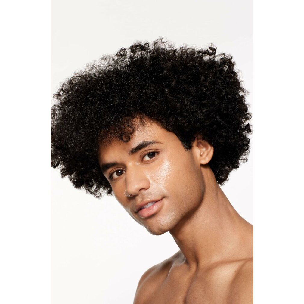 Portrait d'un homme aux cheveux bouclés. Peau avec fond de teint. Regard vers la caméra.