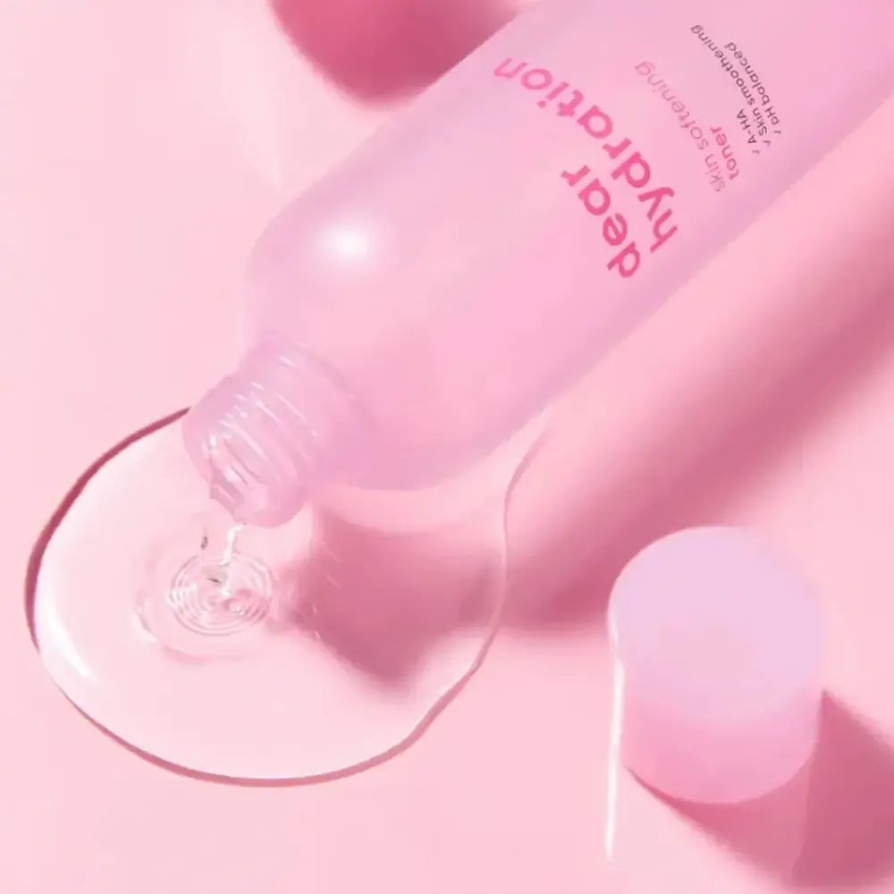 Roze fles, vloeistof wordt uitgegoten. Opschrift: dear hydration, skin softening toner. Merk: BANILA CO.
