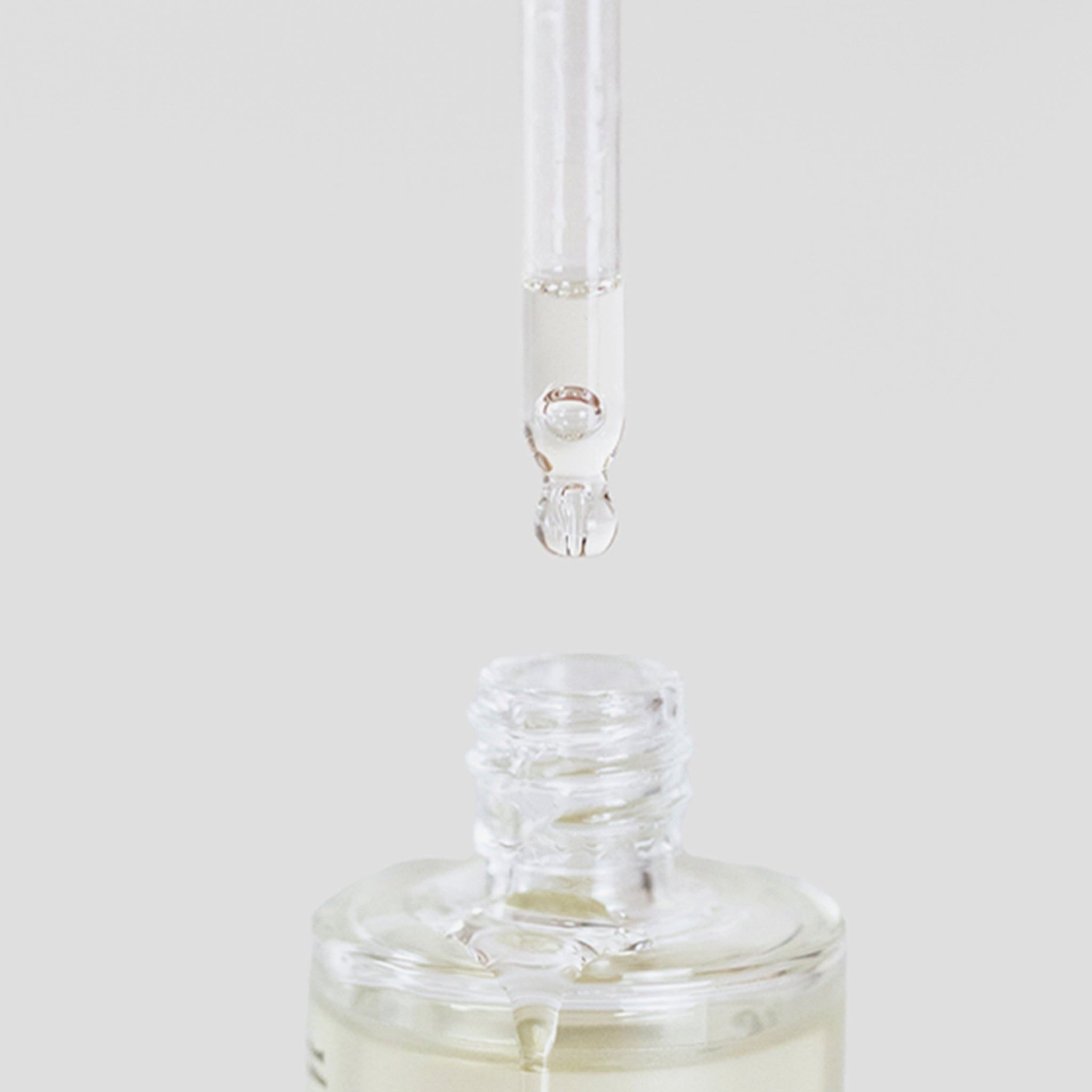 Gros plan d'un flacon en verre avec pipette. Goutte d'huile au bout de la pipette.