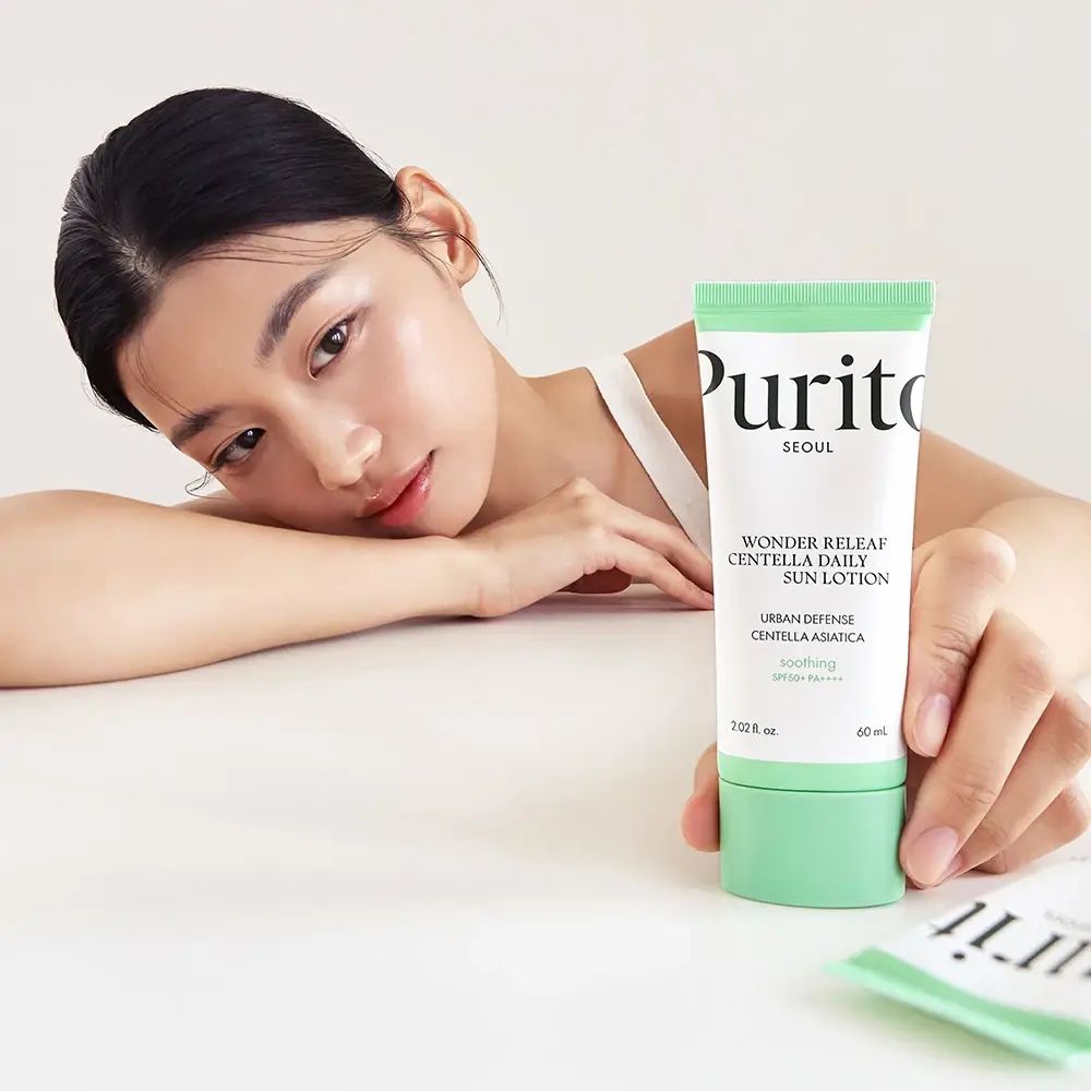 Vrouw houdt een tube Purito Wonder Releaf Centella Daily Sun Lotion vast. Witte top, lichte huid.