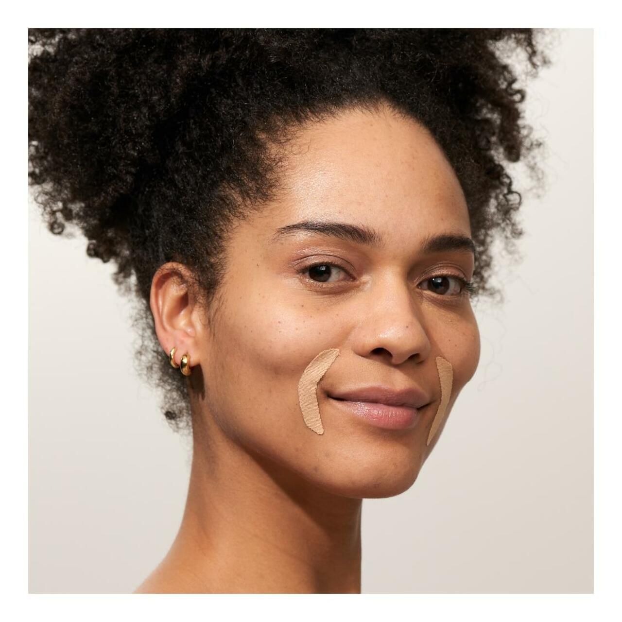 Vrouw met twee mouth patches op de wangen. Patches zijn beige en halvemaanvormig. Vrouw lacht.