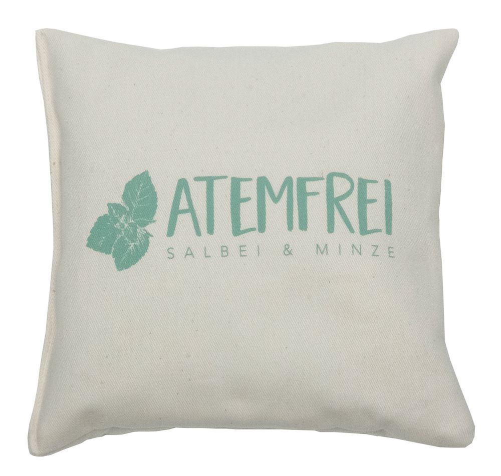 Coussin beige avec inscription "ATEMFREI SALBEI & MINZE" et motif d'herbes vertes. Forme carrée.