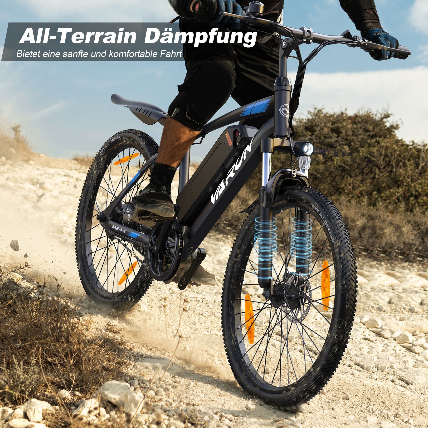 E-bike in beweging op oneffen terrein. Zichtbaar: VARUN, vering, oranje reflectoren, zwarte banden.