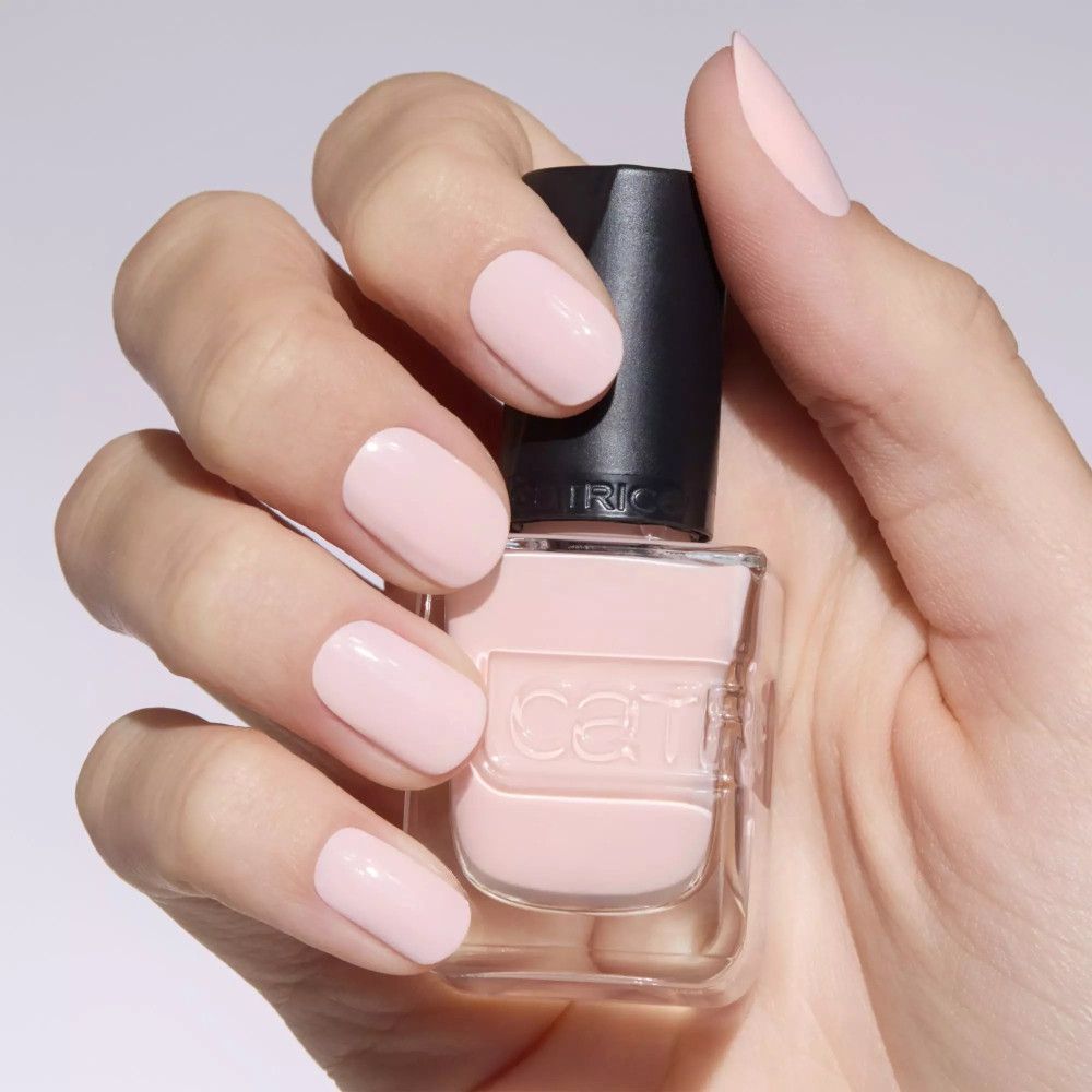 Main avec ongles vernis et flacon de vernis. Vernis rose, bouchon noir. Marque Catrice.
