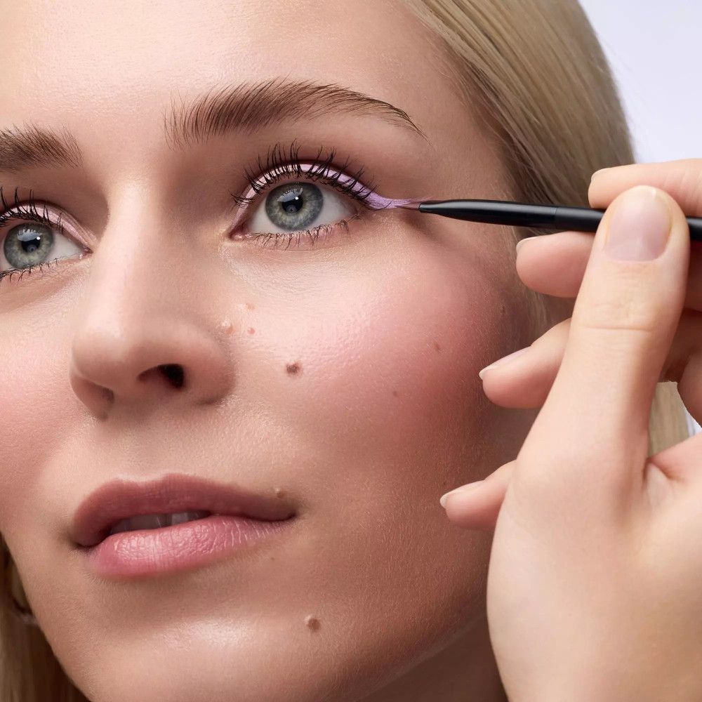 Gros plan sur un œil maquillé avec un pinceau eyeliner. Pinceau en main, traçant une ligne.