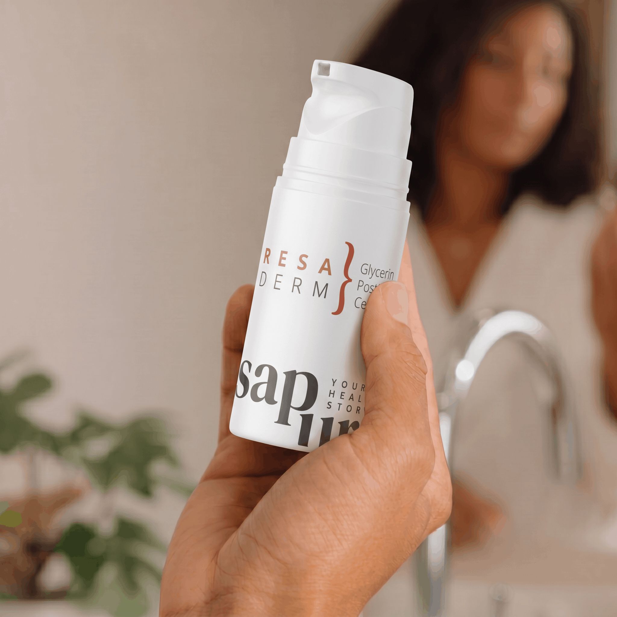 Une main tient un flacon pompe blanc de crème pour rosacée devant un miroir de salle de bain.