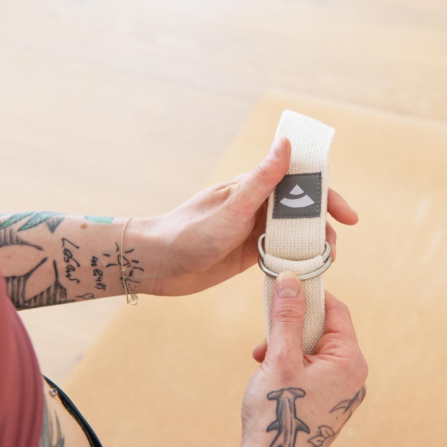 Personne tenant une sangle de yoga beige. Anneau métallique et logo visibles.