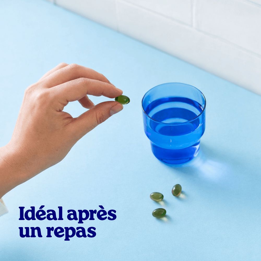 Main tenant une gélule L-Théanine Oméga-3 au-dessus d'un verre bleu.