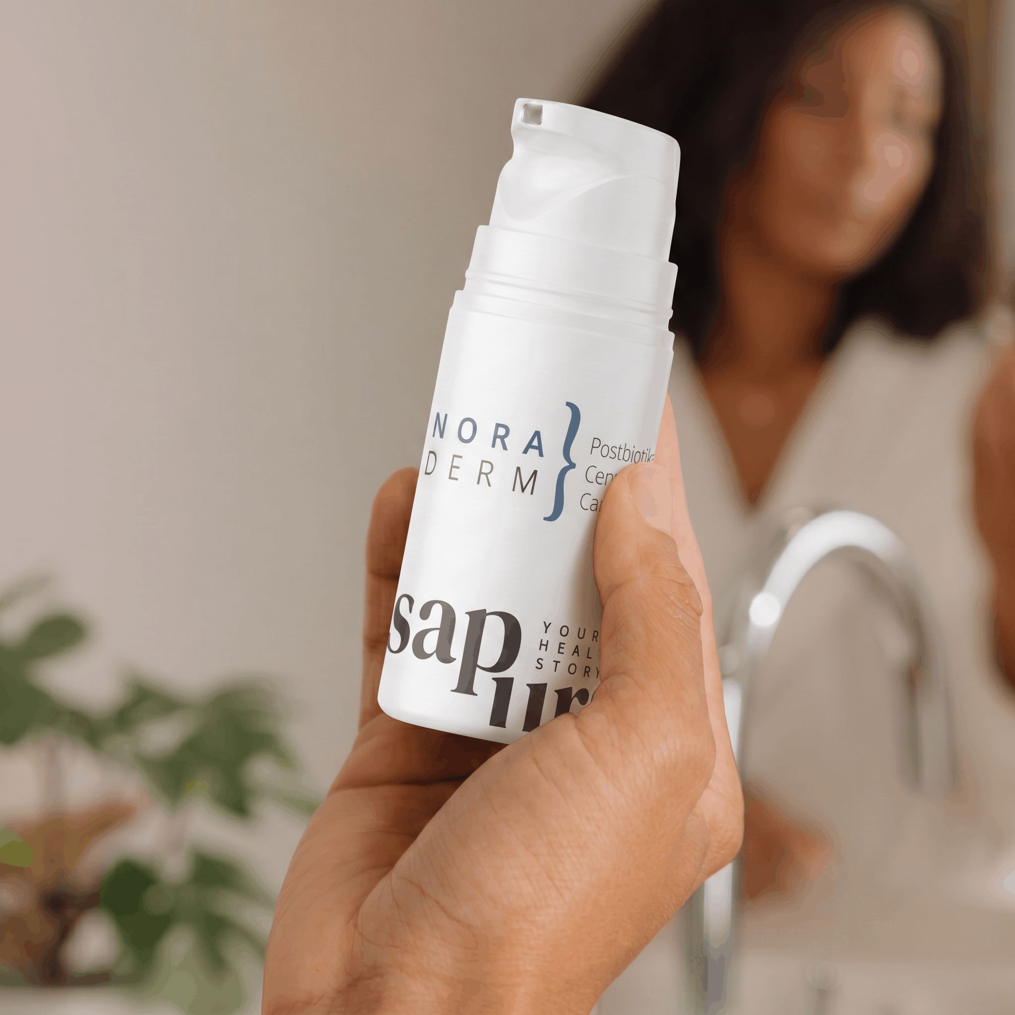 Hand houdt witte fles met pompdosering, opschrift 'NORADERM' en 'sapura', voor een spiegel.