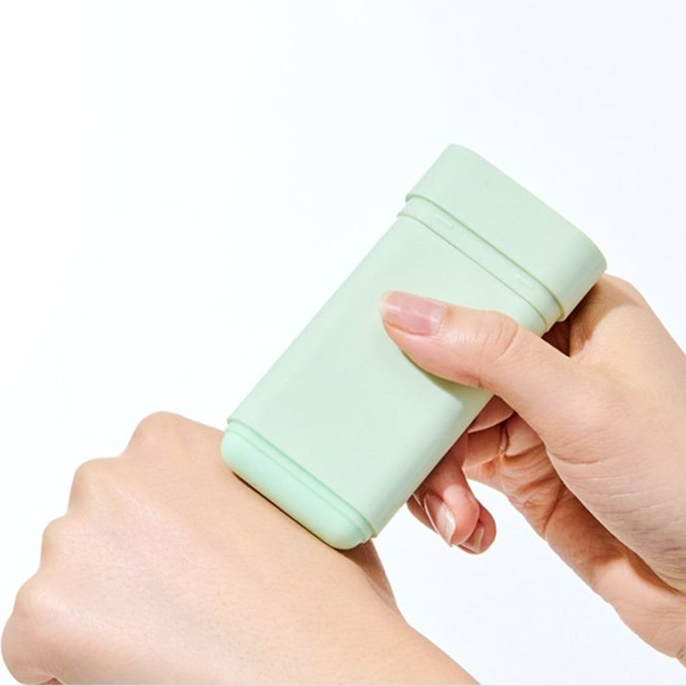 Een hand houdt een lichtgroene zonnebrandstick vast. De stick wordt op de huid aangebracht.