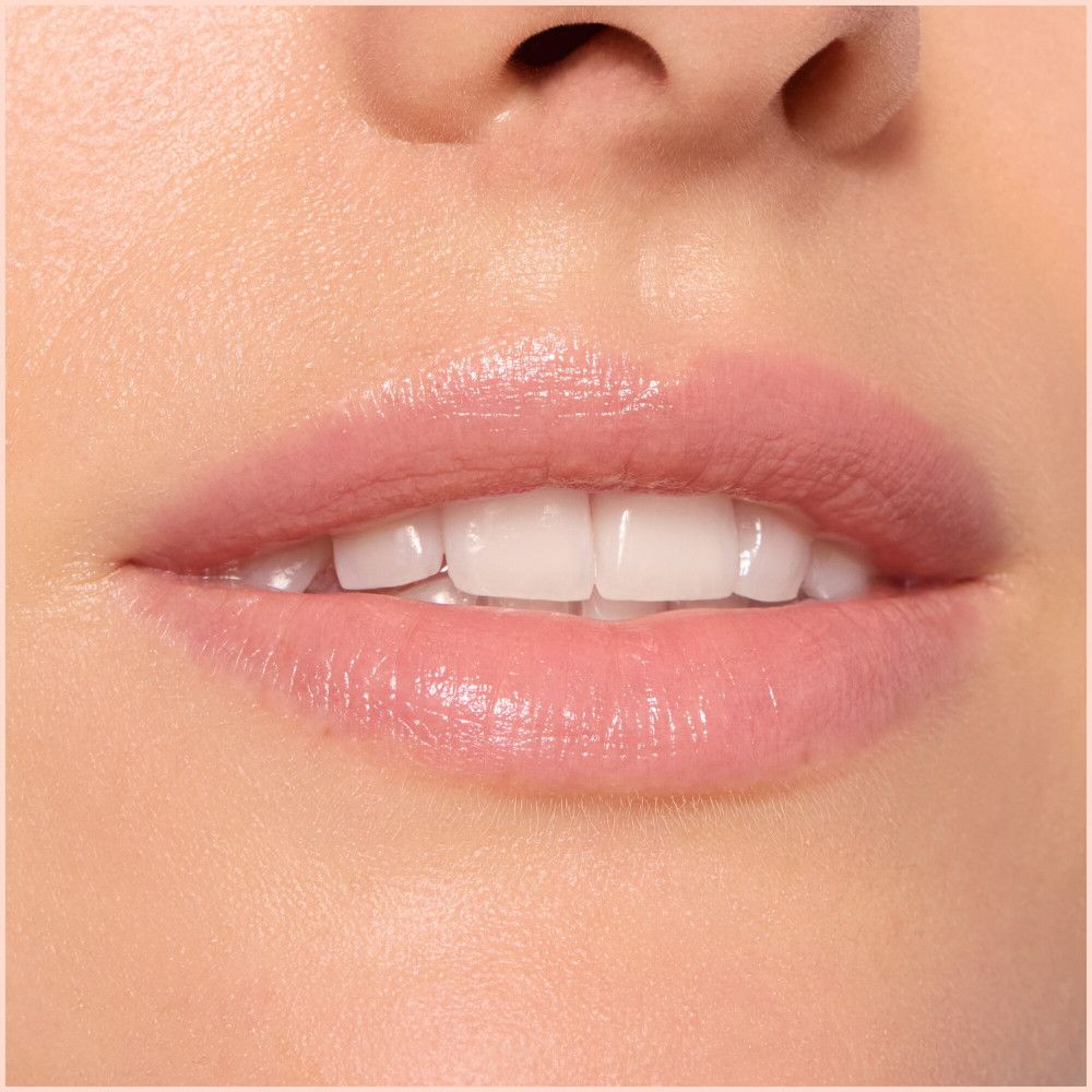 Gros plan sur les lèvres. Les lèvres sont recouvertes de baume à lèvres, ce qui leur donne un effet brillant. Les dents blanches sont visibles.