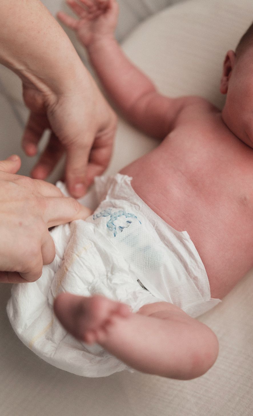 Baby krijgt een luier om. Witte luier met blauw wolkenpatroon.