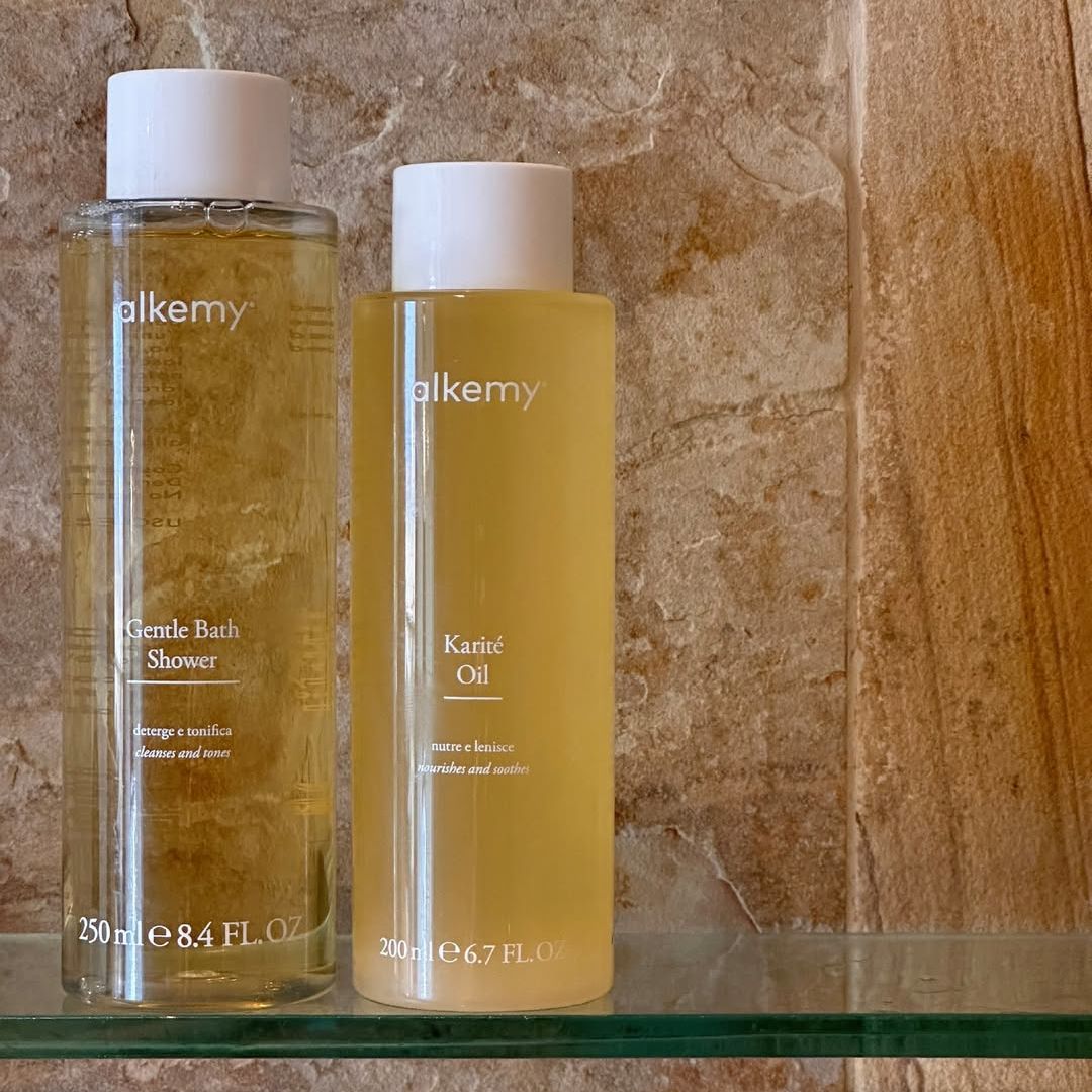 Deux bouteilles Alkemy : gel douche (250ml) et huile de karité (200ml) sur une étagère.