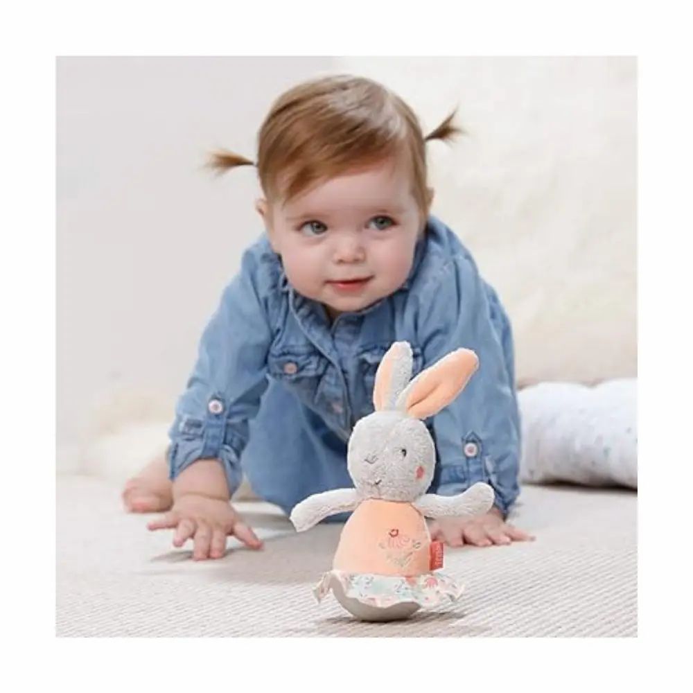 Baby kruipt naar een grijs knuffelkonijn met roze buik en oren. Merk: Fehn.