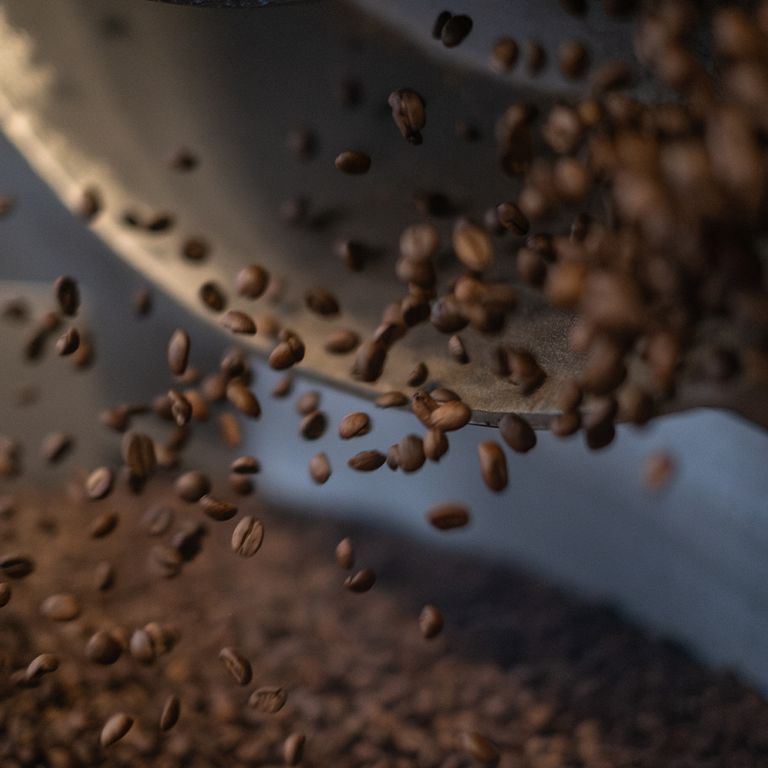 Des grains de café tombent d'un bol en métal. Grains de café bruns en mouvement.